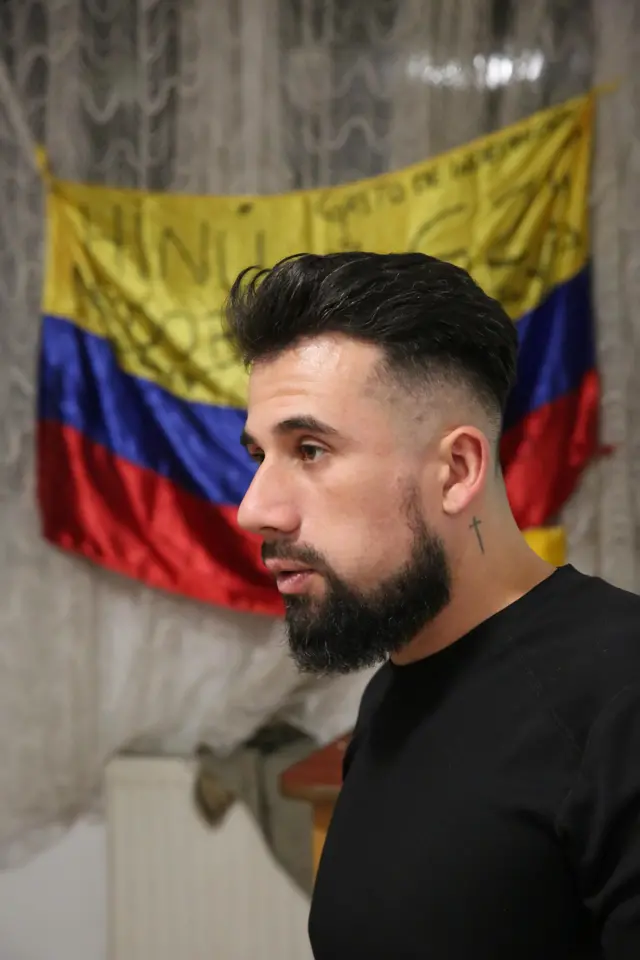 Арабе стоїть у профіль, за ним колумбійський прапор.